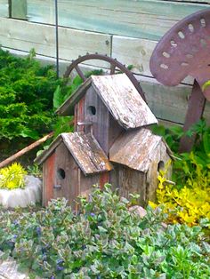 a bird house in the middle of some flowers and plants next to a wooden fence