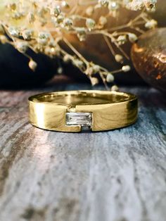 a gold wedding band with a baguette cut diamond set in the center on a wooden surface