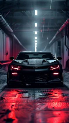 the front end of a black sports car parked in a garage with red lights on it