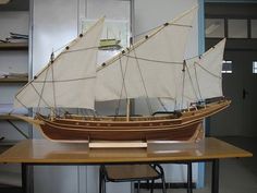 a model sailboat sitting on top of a wooden table next to a book shelf