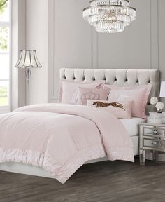 a bed with pink comforter and pillows in a room next to a chandelier