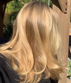 the back of a woman's head with long blonde hair in front of a wooden structure