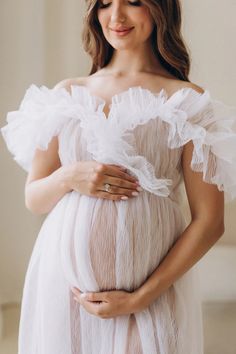 a pregnant woman wearing a white dress and holding her belly