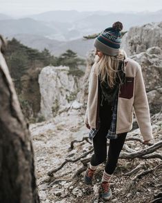 a woman standing on top of a mountain next to a tree