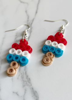 two pairs of earrings with red, white and blue beads are on a marble surface