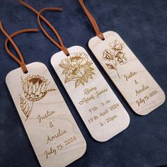 three wooden tags with names on them sitting on a blue cloth covered surface, one has a brown string and the other has a flower