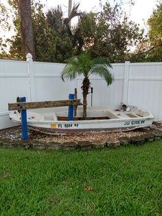 a small white boat sitting on top of a lush green field next to a fence