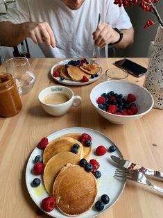 a man sitting at a table eating pancakes and berries