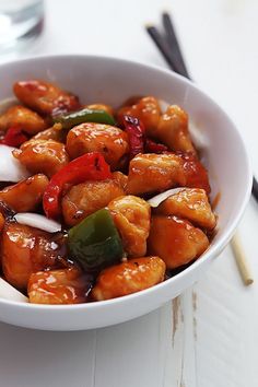 a white bowl filled with chicken and vegetables on top of a table next to chopsticks