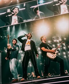 three men are performing on stage with guitars in their hands and one man is singing into the microphone