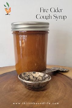 a wooden table topped with a mason jar filled with liquid next to a metal spoon