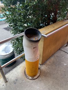 a trash can sitting on the side of a sidewalk next to a fence and tree