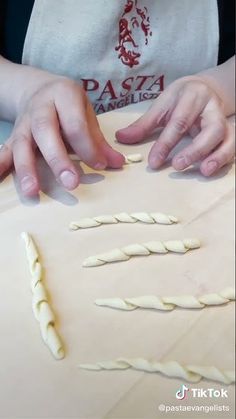 two hands are on top of some dough and rolling it into spirals to make pasta