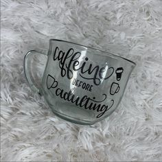 a glass cup that says caffeine before daunting on the side, sitting on a fluffy white surface