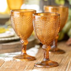 three glass goblets sitting on top of a wooden table next to each other