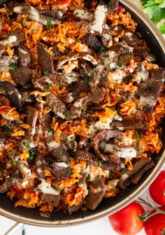 a skillet filled with rice, meat and vegetables on top of a white table