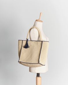 a white mannequin with a black tassell and a beige bag on it