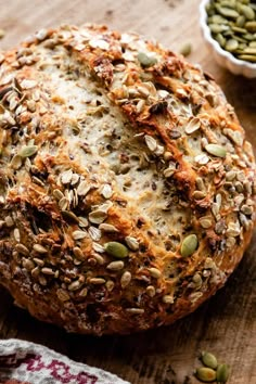 a loaf of bread sitting on top of a wooden table next to two bowls filled with seeds