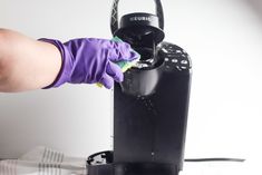 a person in purple gloves is cleaning a black coffee machine with a green glove on it