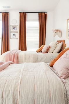 two twin beds in a bedroom with pink and white bedding, brown drapes on the windows