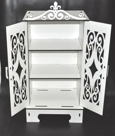 an open white cabinet with ornate designs on the front and sides, against a black background