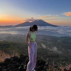 a woman standing on top of a mountain looking out at the clouds in the sky