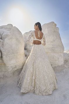 a woman in a white wedding dress standing next to large rocks and looking off into the distance