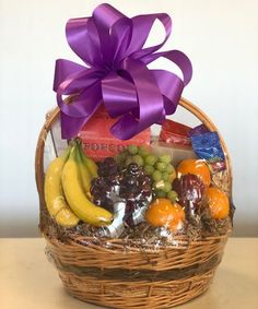 a wicker basket filled with assorted fruit and chocolates, wrapped in purple ribbon