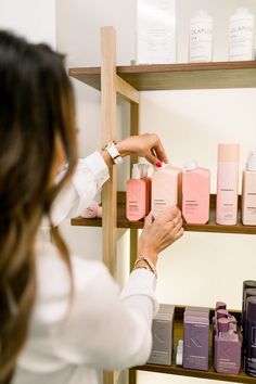 a woman in a white shirt is looking at some pink and purple products on shelves