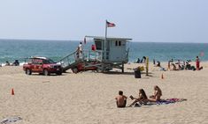 people are sitting on the beach near a life guard tower