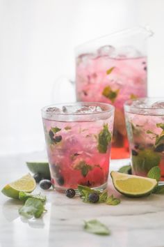 two glasses filled with lemonade, mint and blueberries on a marble counter top