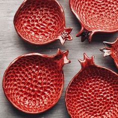 four red ceramic pomegranates sitting on top of a wooden table