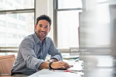 a man sitting at a desk in front of a laptop computer and smiling for the camera