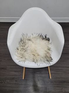 a white chair with a furry rug on it's back and wooden legs in front of a wall