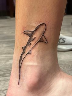 a small tattoo on the ankle of a woman's foot, depicting a shark