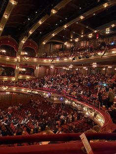 an auditorium full of people sitting and standing in the middle of it with lights on