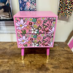 a pink dresser with flowers painted on the front and sides, sitting on top of a wooden table