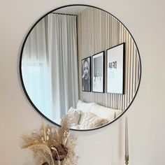 a round mirror hanging on the wall above a vase with dried flowers in front of it