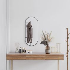 a table with a mirror, vase and plants on it in front of a white wall