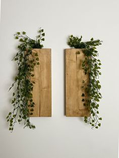 two wooden boards with plants on them hanging from the wall next to each other in front of a white wall