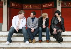 four people are sitting on the steps in front of a building with red shutters