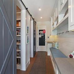 a long narrow hallway with white cabinets and gray walls, leading to the front door