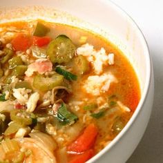 a bowl of soup with shrimp, carrots, and green peppers in it on a white surface