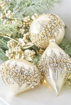 three christmas ornaments sitting on top of a white table next to evergreen branches and pine cones