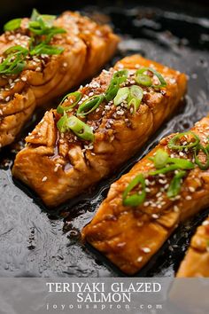 salmon fillets with sesame seeds and green onions on a black plate, ready to be served