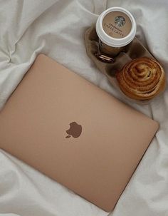 an apple laptop sitting on top of a bed next to a cup of coffee and pastry