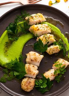 a black plate topped with fish covered in green sauce