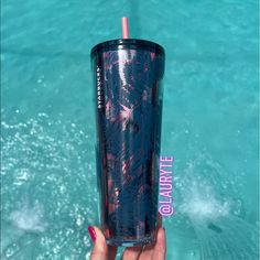 a person holding up a drink in front of the water with palm trees on it