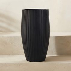 a large black vase sitting on top of a set of steps in front of a wall