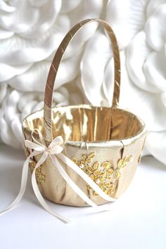 a gold basket with a ribbon tied around it and white flowers in the back ground